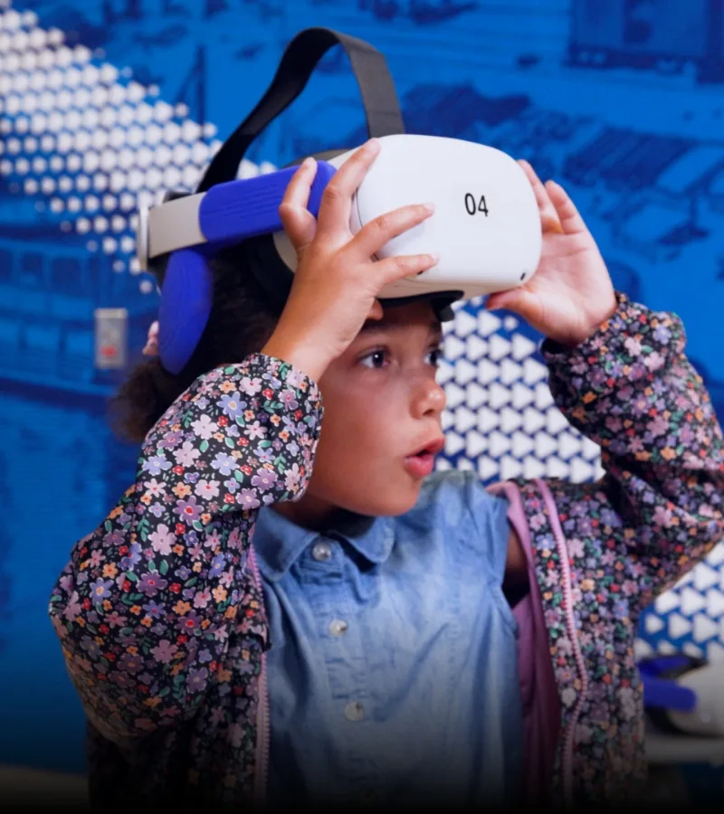 child using VR goggles in front of graphic wall.