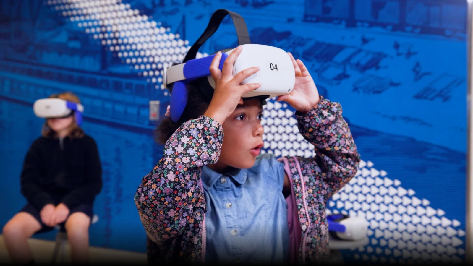child using VR goggles in front of graphic wall.