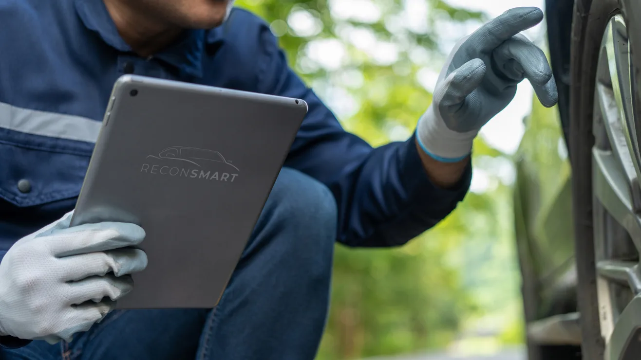 A gloved technician holding a tablet branded with the ReconSmart logo while inspecting a vehicle tire.