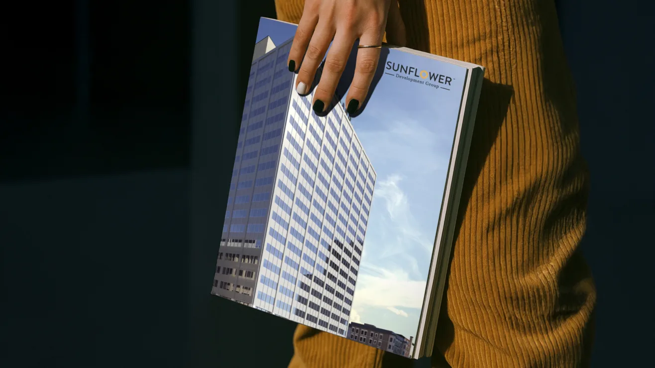 A person holding a printed portfolio brochure featuring a high-rise building and the Sunflower Development Group logo.